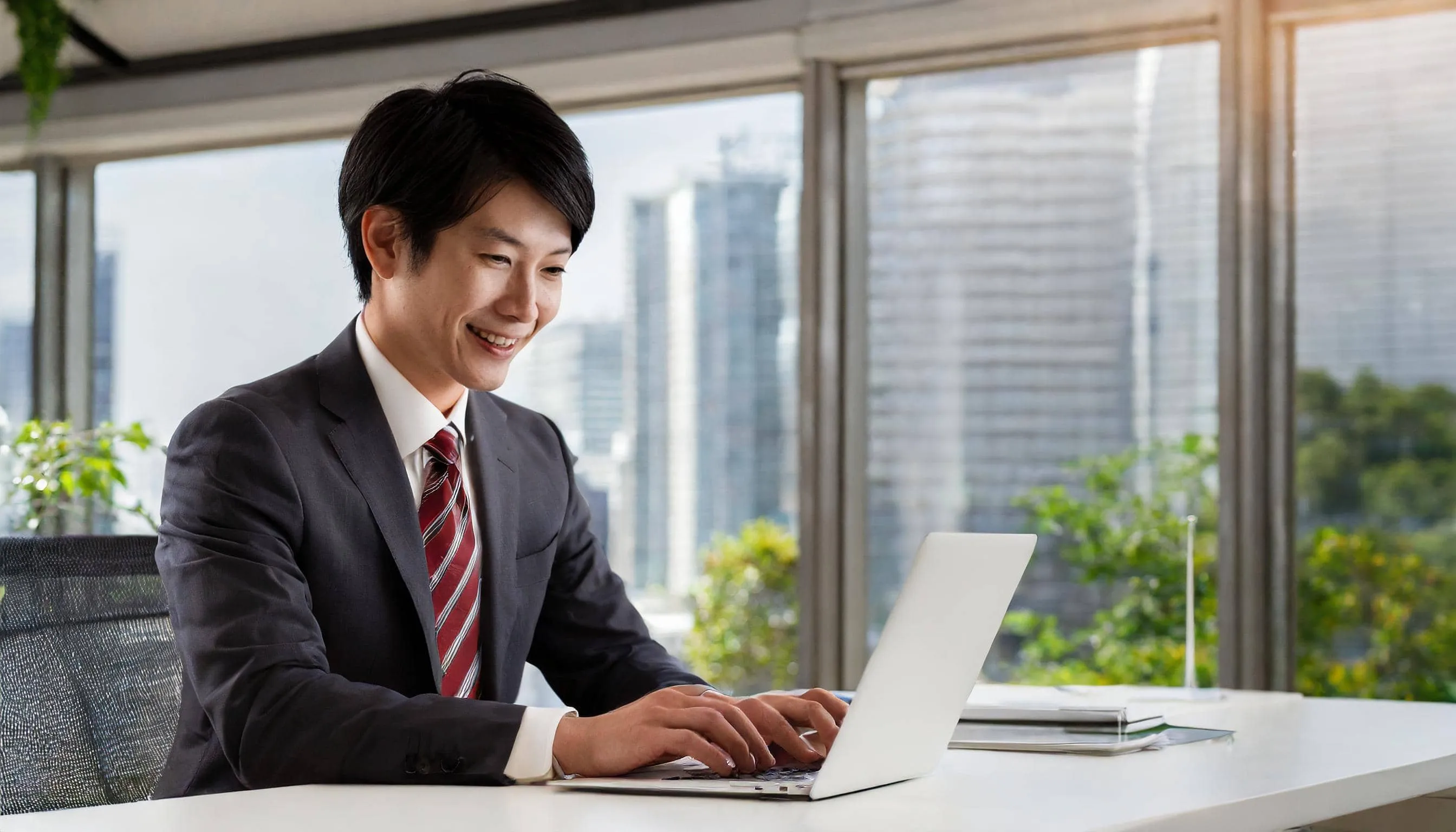 明るいオフィスでノートパソコンに向かい笑顔で提案資料を作成する男性営業スタッフ